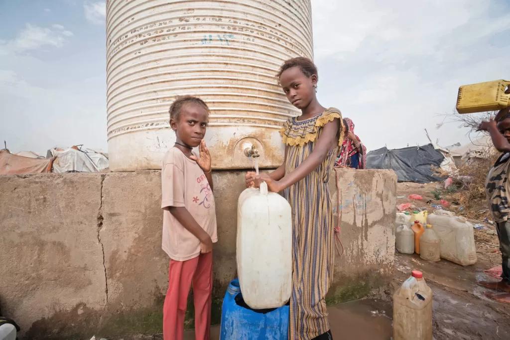 Cousins aged 7 and 11 collecting water from a water storage tank.